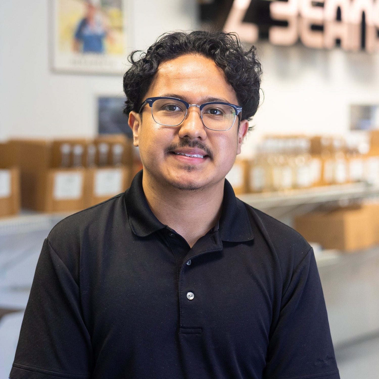 Man wearing glasses and a black shirt in a store setting with shelves and branding in the background