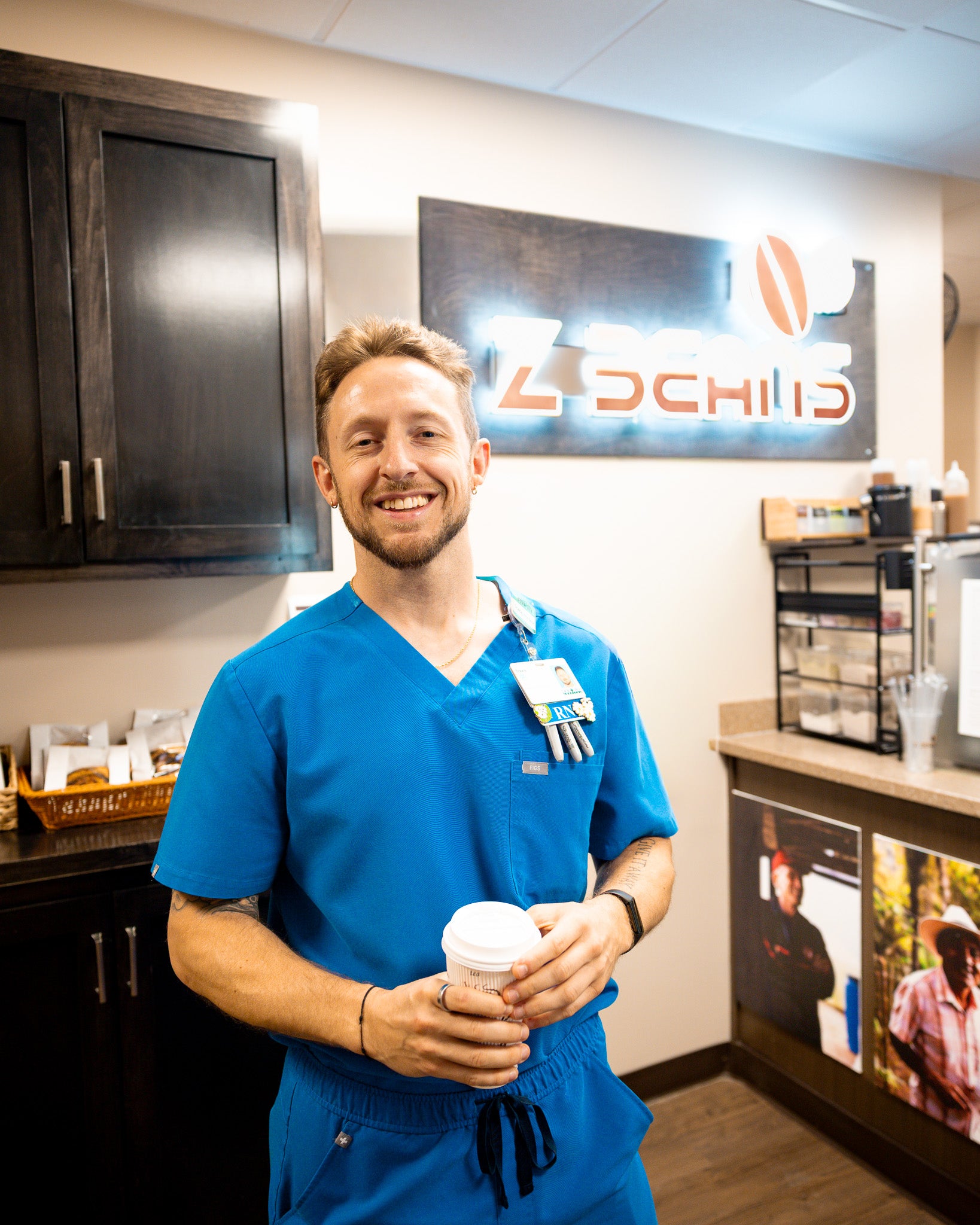 Man in blue scrubs holding a coffee cup in a hospital cafe setting with 'Z Beans' branding.