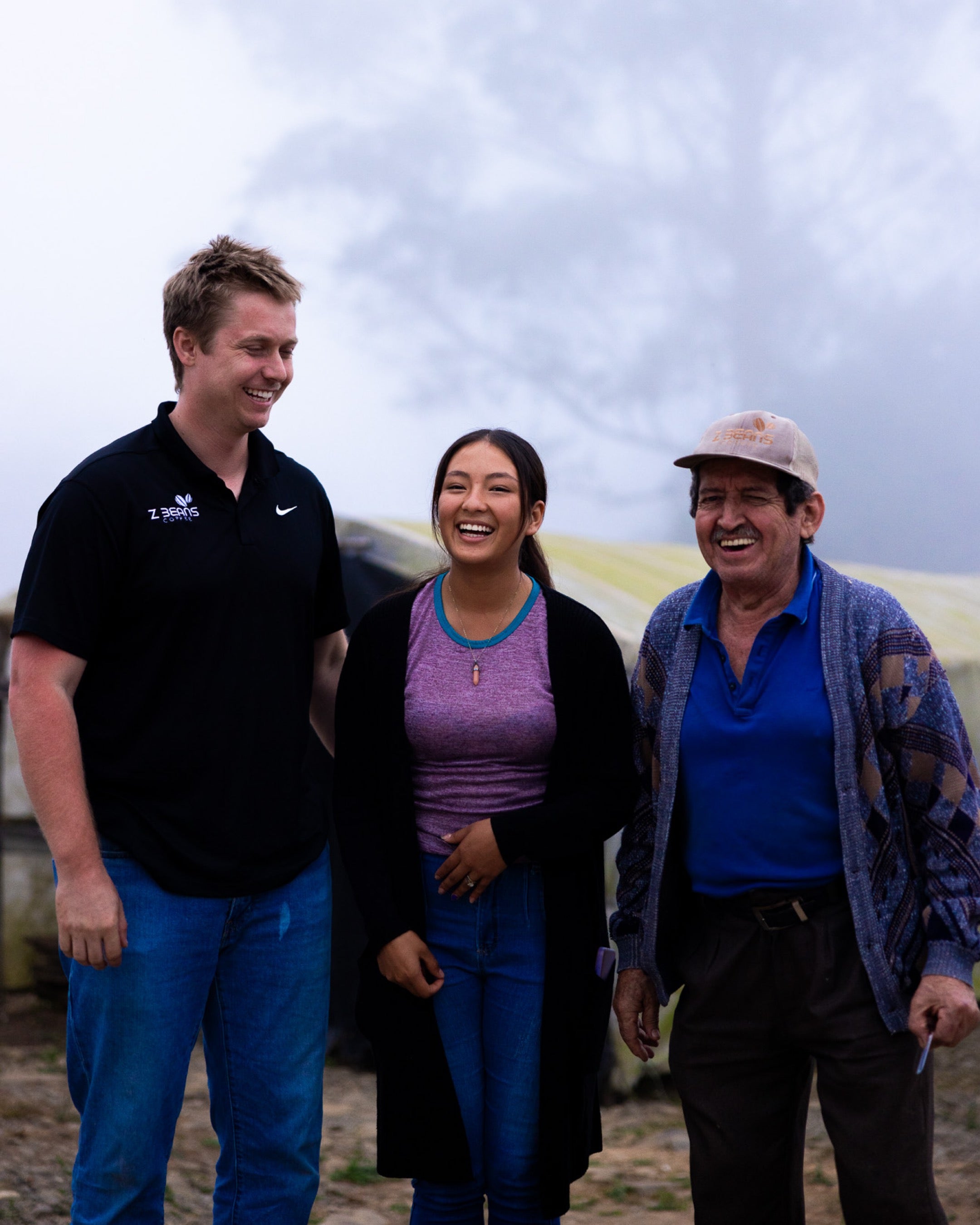 Three people standing together outdoors with a cloudy sky in the background