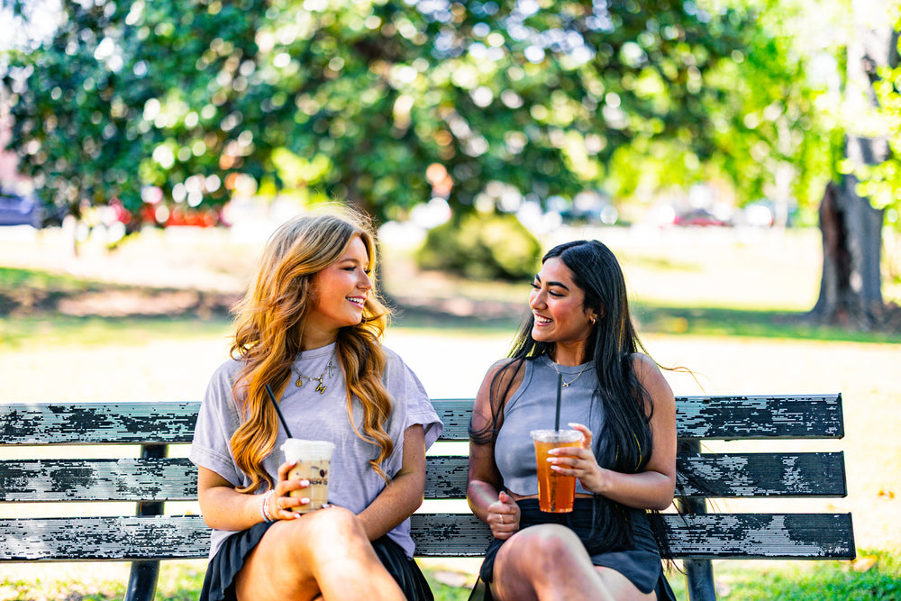 Two women sitting on a park bench enjoying drinks.