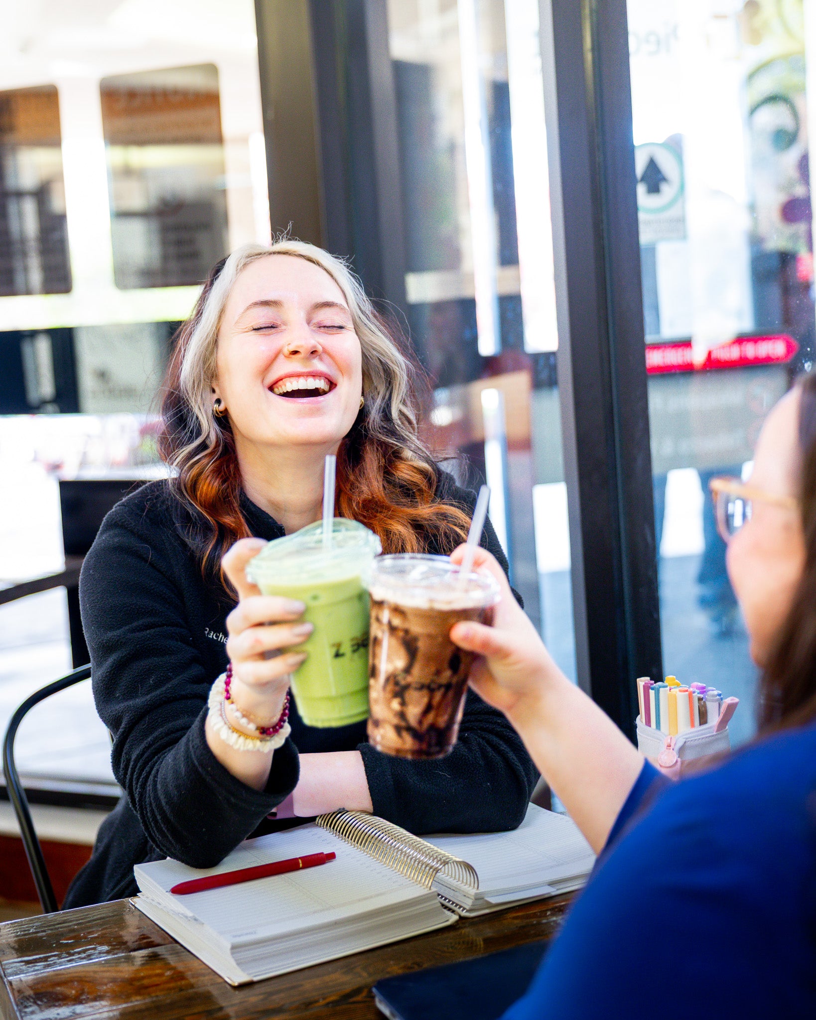 Girl in black jacket drinking a matcha and laughing