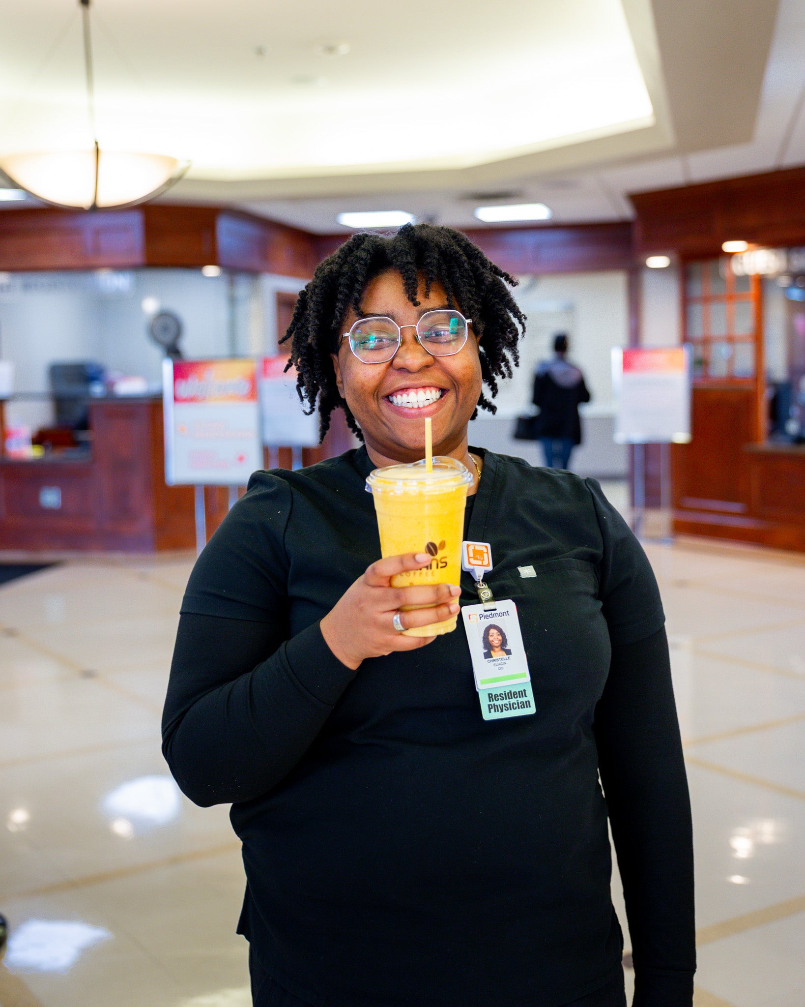 Woman wearing black drinking a peach smoothie in a hospital lobby
